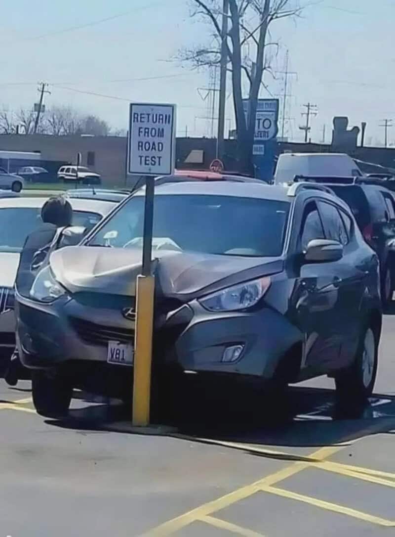 Car crashed into a yellow pole in a parking lot with a "Return from Road Test" sign.