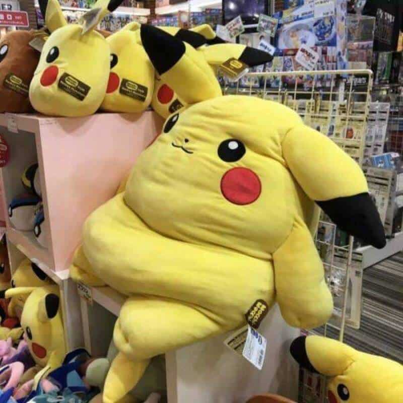 Pikachu plush toy sitting on a shelf in a store, surrounded by other Pikachu plushies and merchandis.