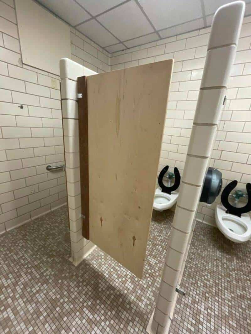 Portable toilet stall with a wooden door in a public restroom.