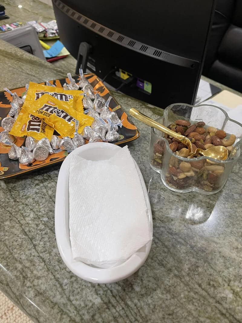Assorted chocolates and nuts on a tray, a tissue box, and a glass container with a spoon on a counte.