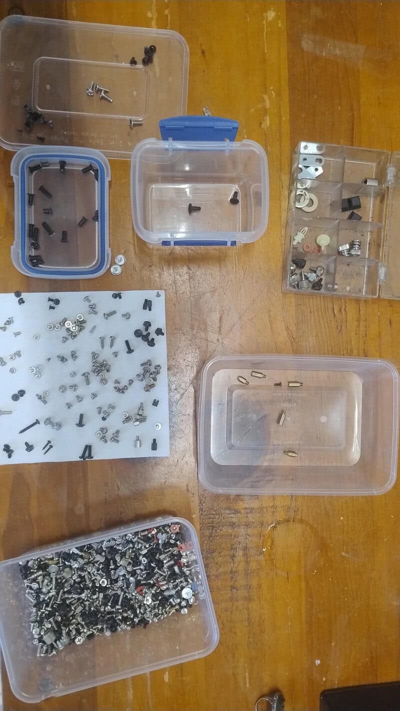 Small plastic containers with various screws, nuts, and small hardware parts on a wooden surface.