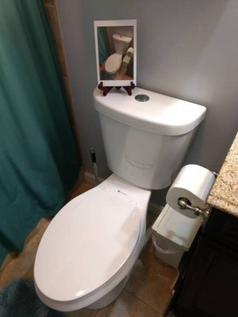 Toilet with a mirror on top showing a reflection of the toilet seat and lid.