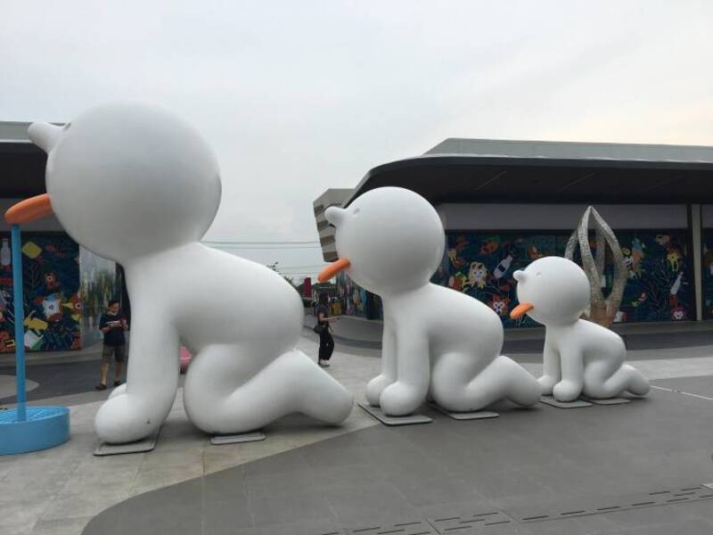 Large snowman sculpture with three smaller snowmen, located outdoors in front of a colorful building.