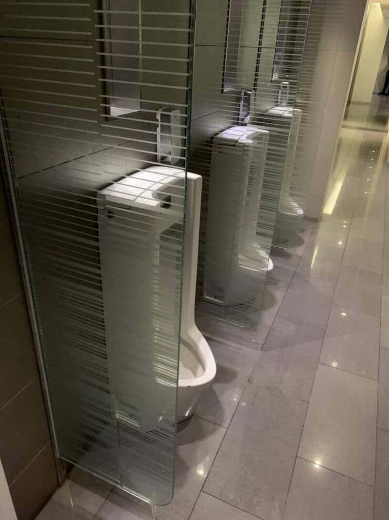 Toilet behind a glass partition with frosted stripes in a public restroom.