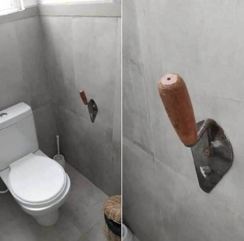 Toilet with a knife embedded in the wall above it, and a wooden handle attached to a metal plate on.