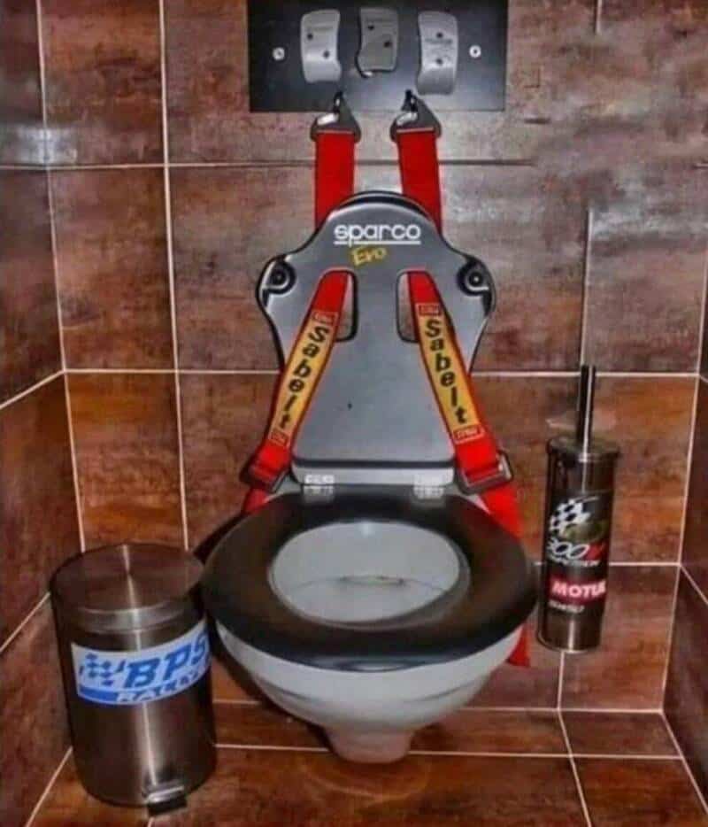 Racing seat mounted on a toilet with "Sabelt" harnesses and racing accessories.