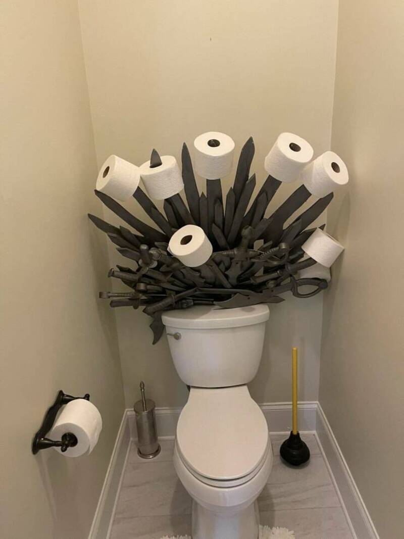 Toilet with a decorative arrangement of toilet paper rolls and black sticks resembling a bouquet, pl.