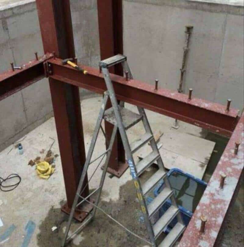 Steel beam construction with bolts and a ladder inside a building under construction.