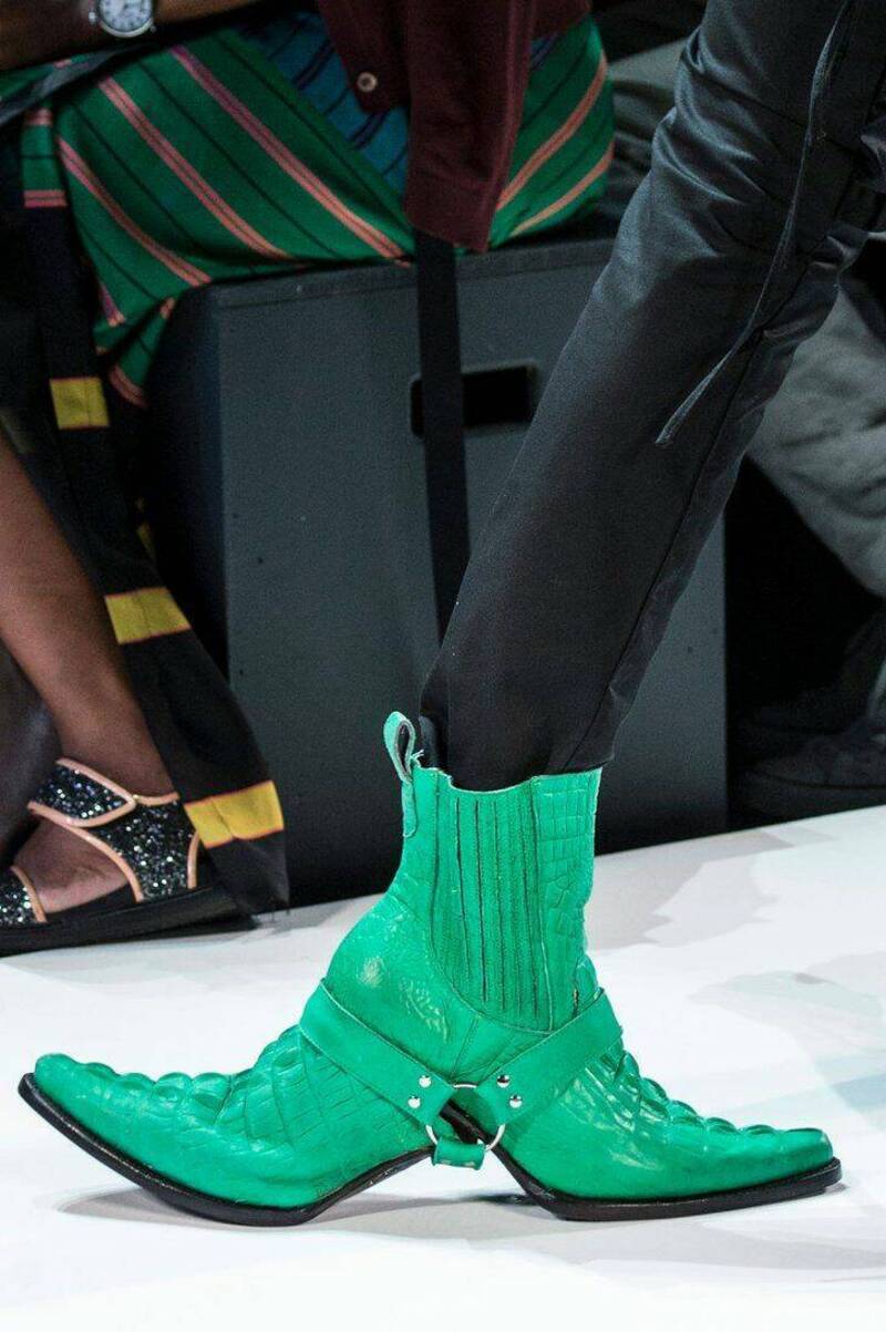 Green high-heeled boots with a strap and buckle detail, worn with black pants.