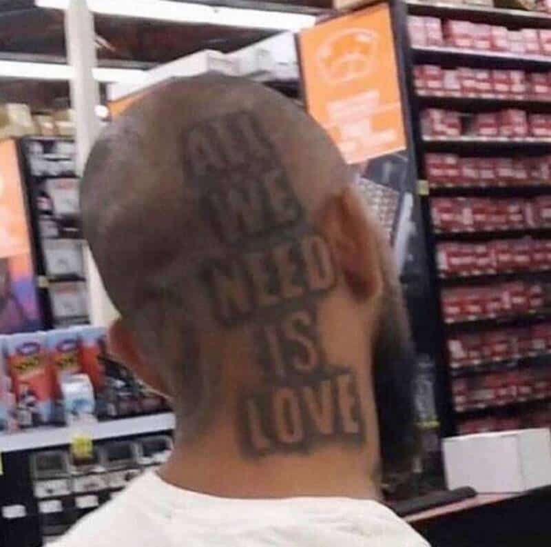 Man with tattooed head reading "All I Need Is Love" in a store aisle.