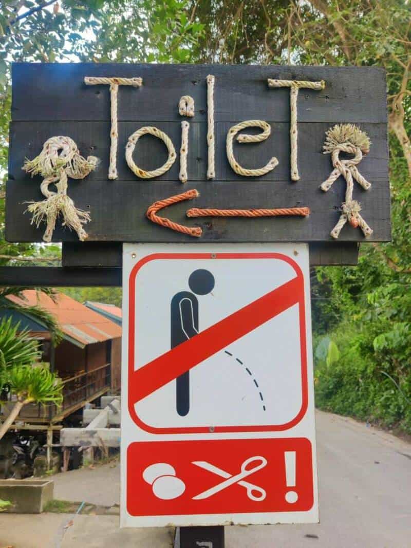 Toilet sign with decorative rope figures and a directional arrow, indicating the location of the toi.
