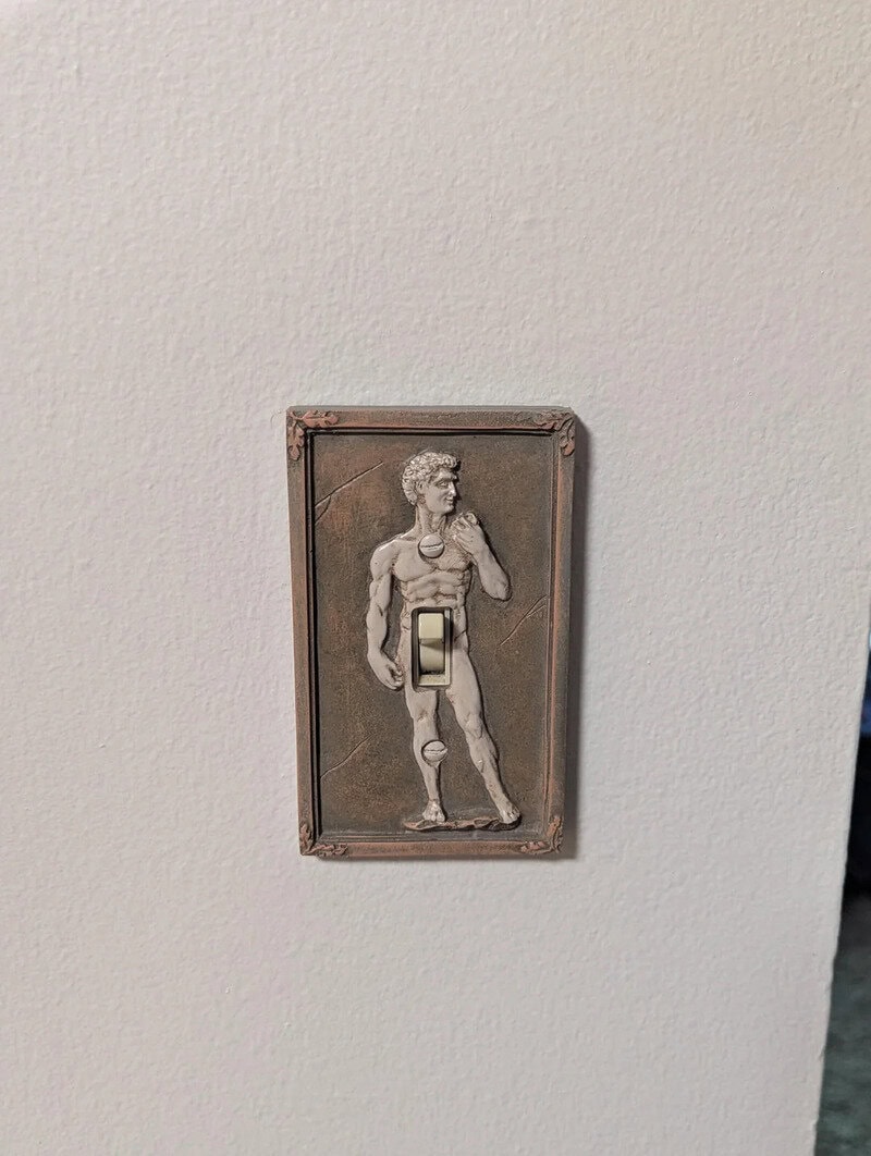 Light switch cover featuring a carved image of a muscular man in a classical pose.