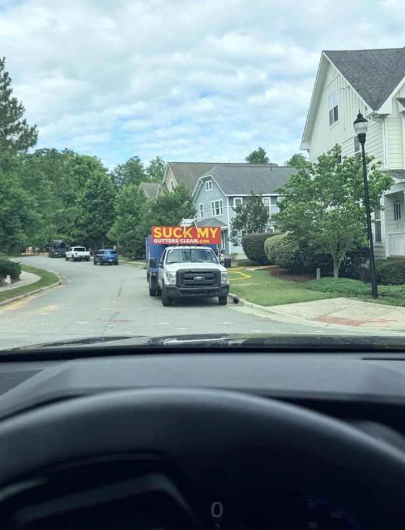 Truck with a sign that says "SUCK MY BUTTER CREAM" on a suburban street.