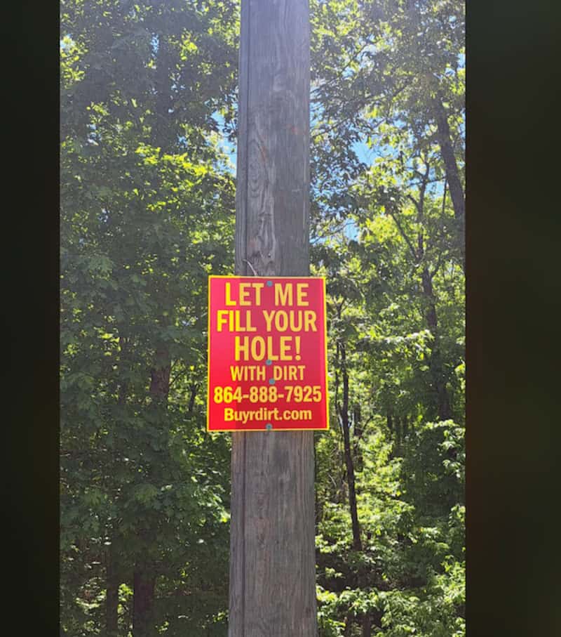 Sign on pole says 'Let me fill your hole! with dirt 864-888-7925 Buydirdirt.com'.