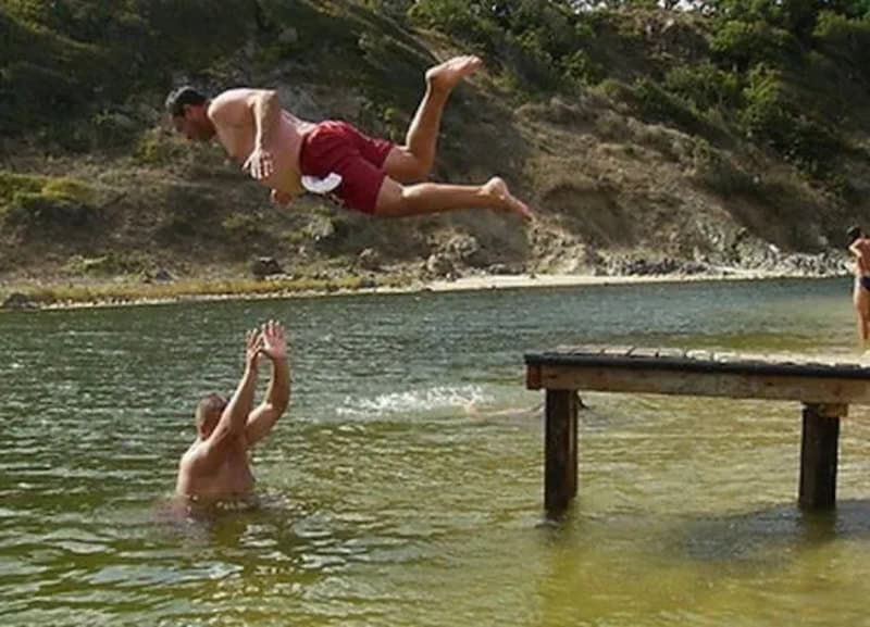 Person jumping into water while another person watches from the water.