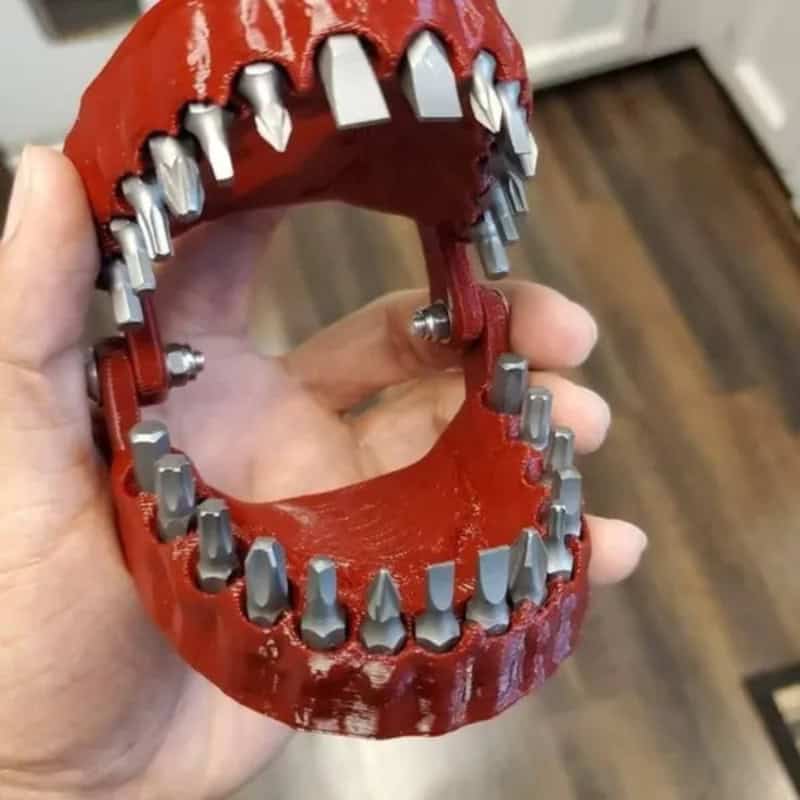 Red plastic toy with metal teeth resembling a mouth, held in hand.