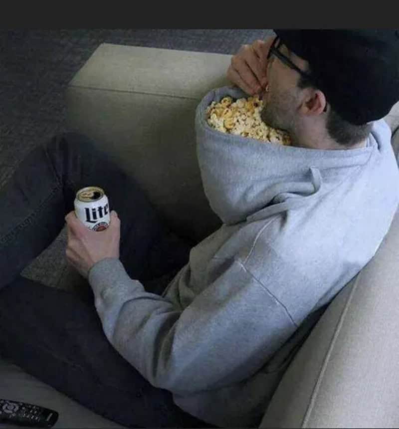 Man in gray hoodie eating popcorn and holding a Miller Lite beer can.