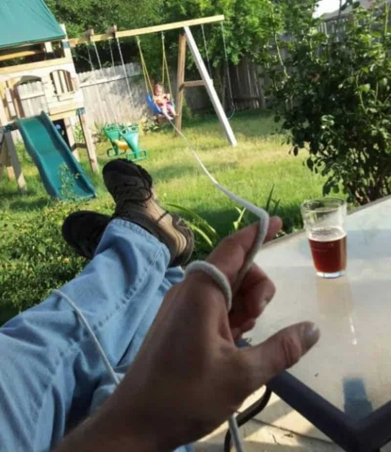 Person relaxing outside with feet up, holding a phone, with a swing set and child in background.