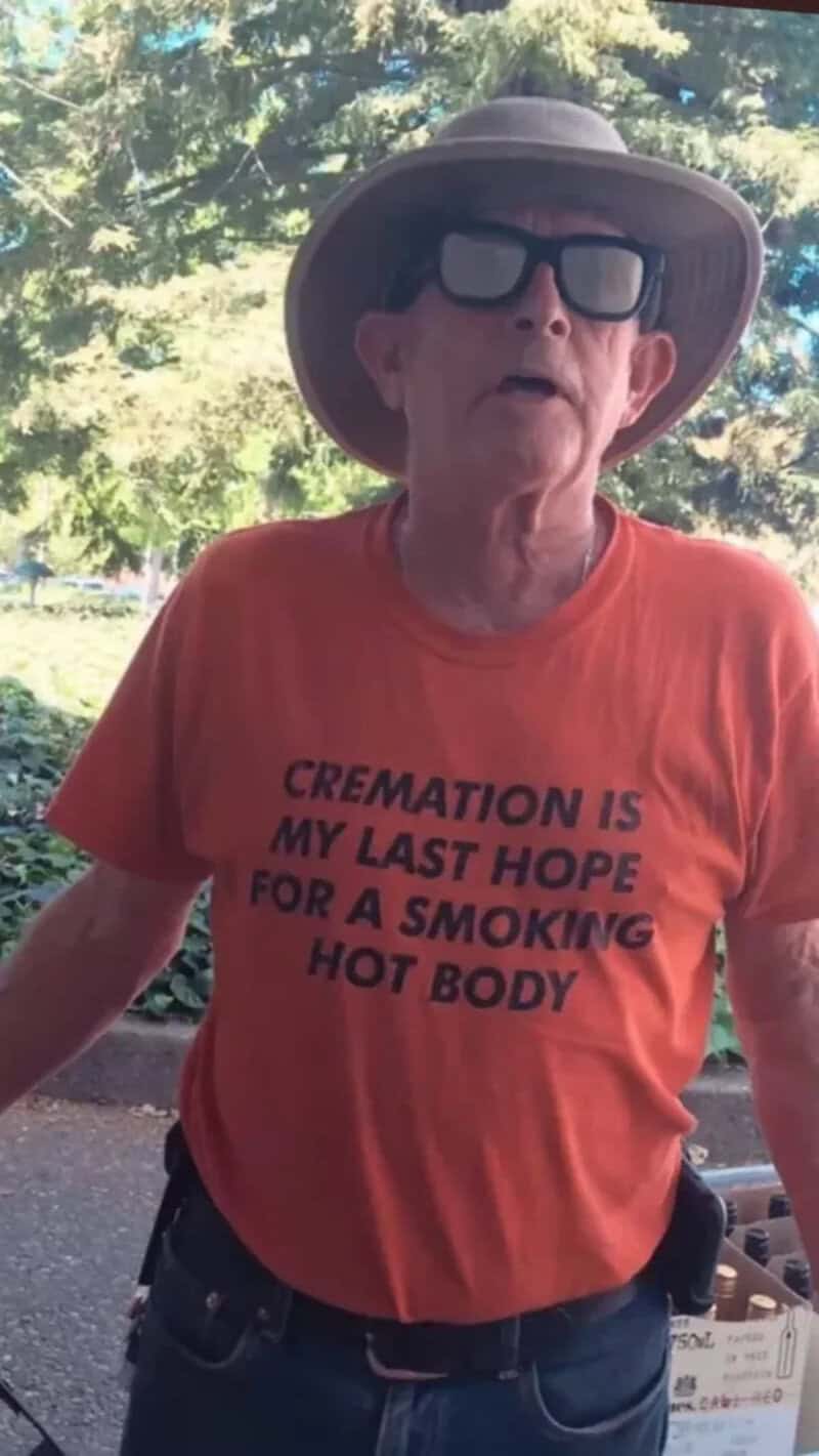 Elderly woman wearing sunglasses and a wide-brimmed hat outdoors, wearing an orange T-shirt.