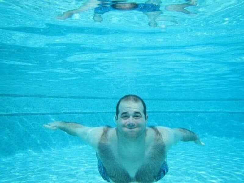 Man swimming underwater with arms outstretched and a smile.