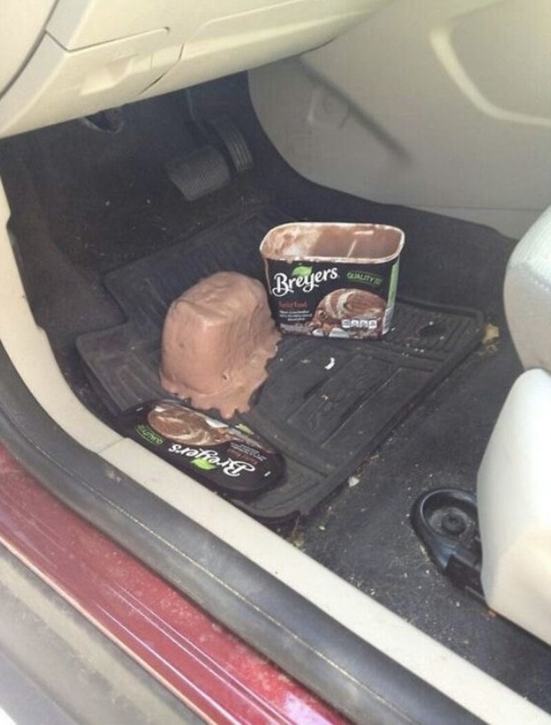 A scoop of Breyers ice cream on a car floor mat with ice cream containers nearby.
