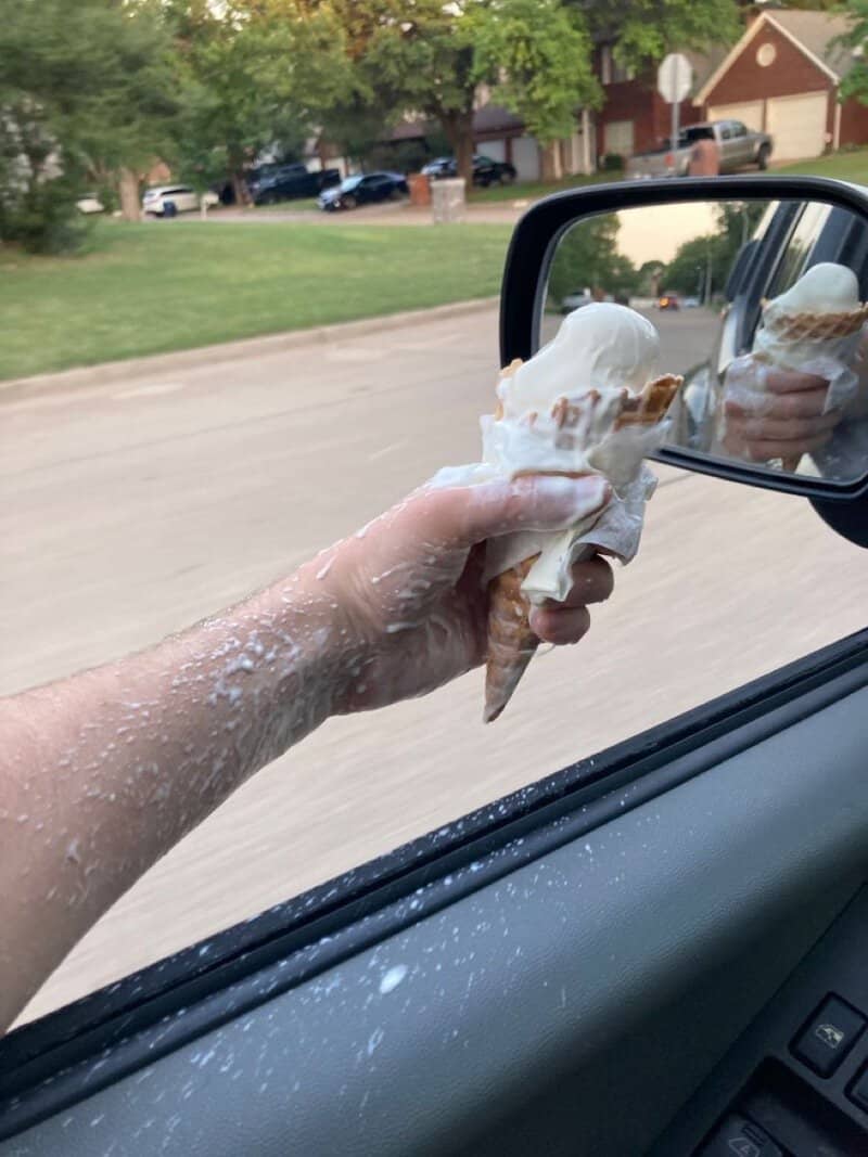 Person's arm with ice cream on it reaching out of car window, ice cream in hand.