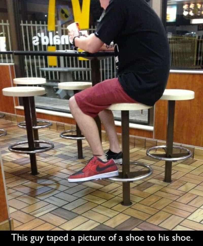 Man at a fast food restaurant taping a picture of a shoe to his shoe.