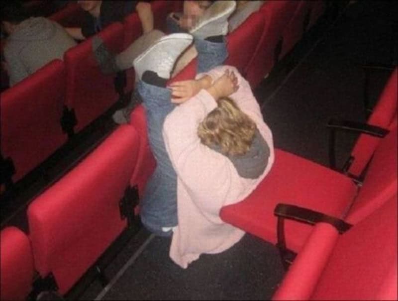 Child lying on theater seat with legs up, head on seat, and arms around knees.