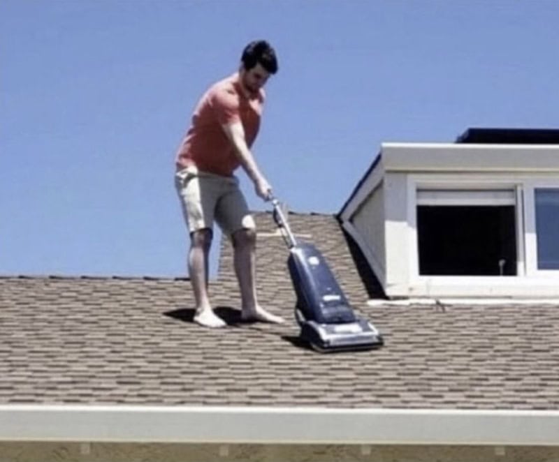 Person vacuuming roof with a small vacuum cleaner on a sunny day.