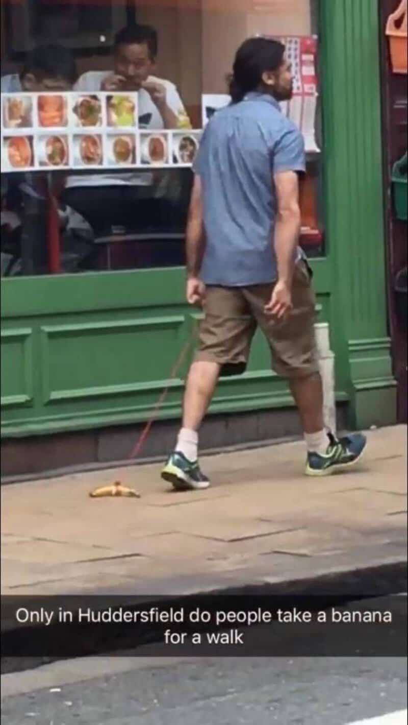 Man walking a dog with a banana on a leash outside a store.