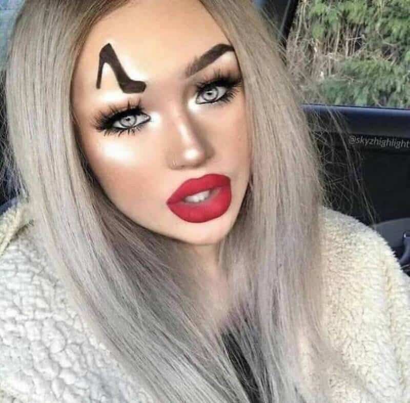 Woman with platinum blonde hair, bold makeup, and a tattoo of a high heel on her forehead.