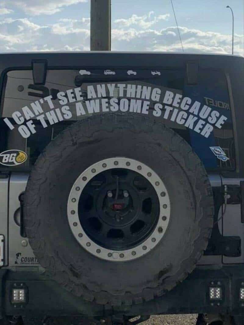 Back of a vehicle with a sticker that says, "I CAN'T SEE ANYTHING BECAUSE OF THIS AWESOME STICKER".