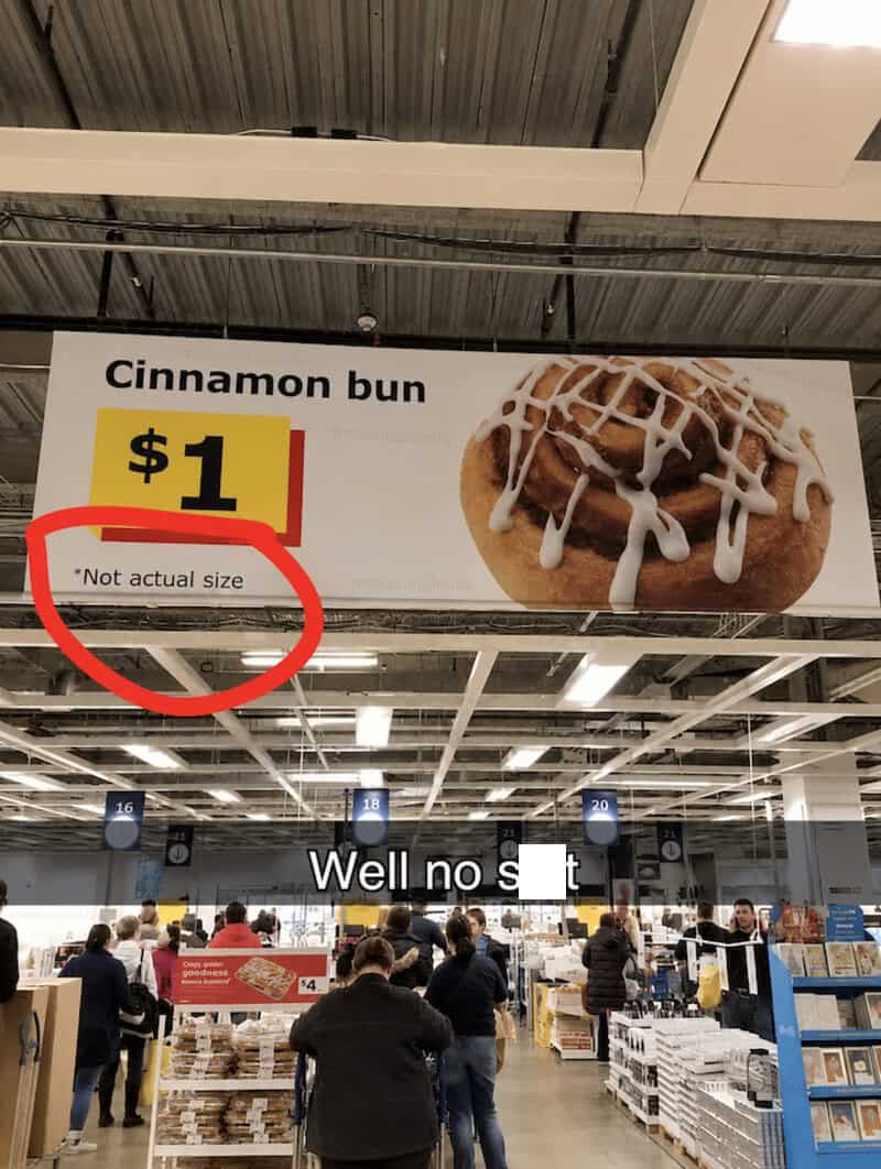Sign for cinnamon bun priced at $1 with 'Not actual size' note, in a busy store.