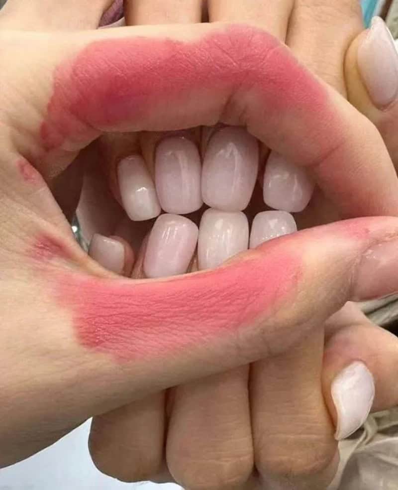 Close-up of a person's mouth with lipstick and teeth showing.