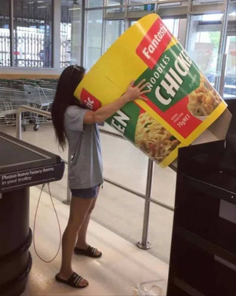Girl pushing a giant cup of instant noodles at a store.