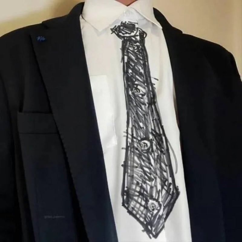 A person in a suit with a white shirt and a black jacket, wearing a hand-drawn tie.