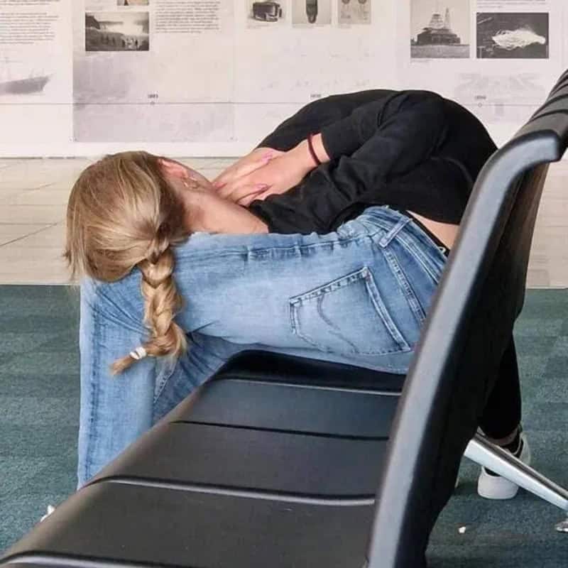 Two women are resting their heads on each other's shoulders in a waiting area.