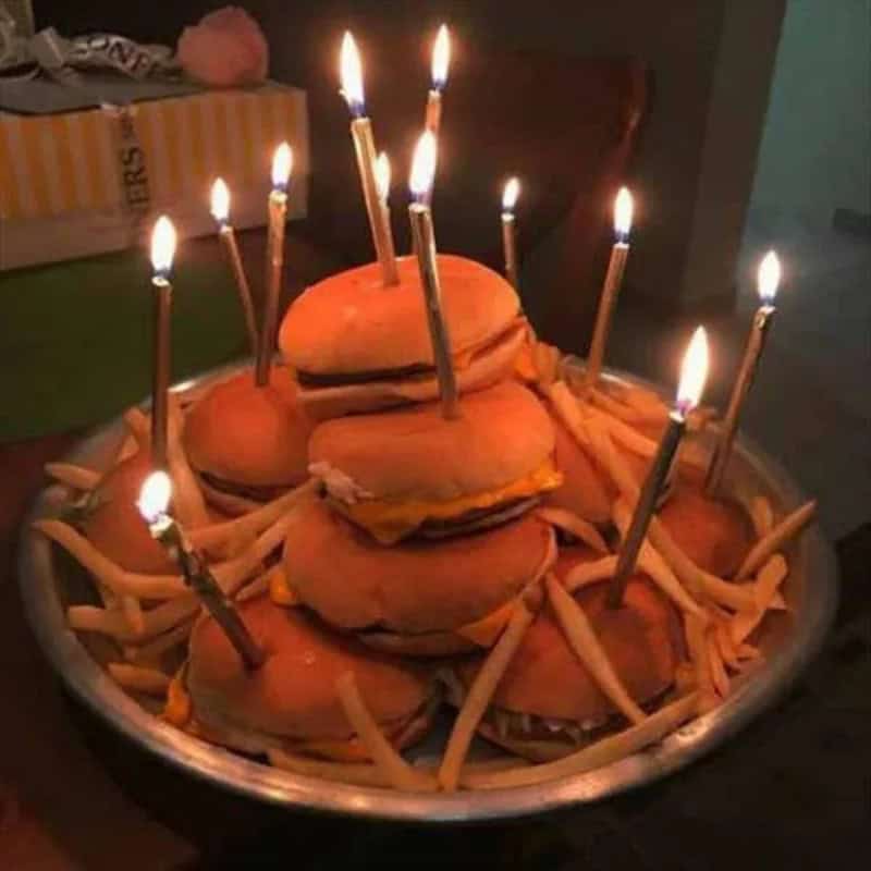 Hamburger-shaped birthday cake with lit candles on top.