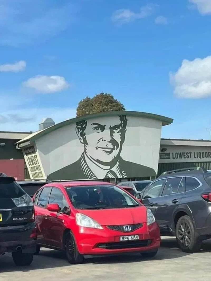 Large mural of a man in a suit on a building, with cars parked in front.