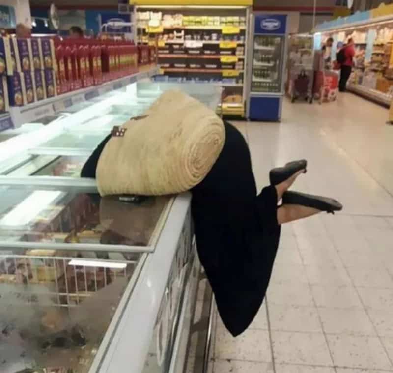 Person with a large rolled-up carpet on their back leaning over a store counter.