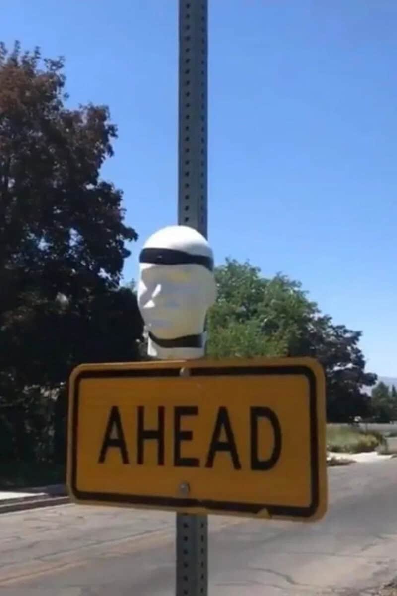 Humorous street sign with a helmeted figure on top of a yellow 'AHEAD' sign.
