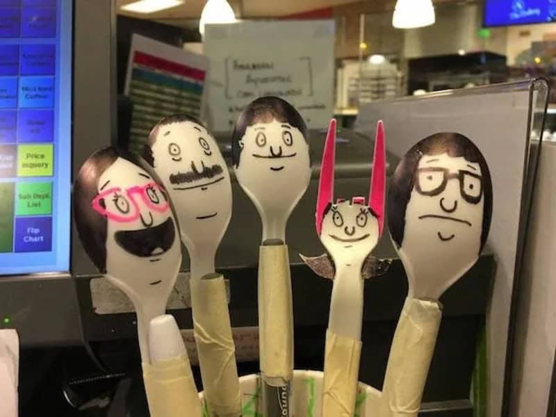 Five decorated spoons with faces and accessories on a store counter.