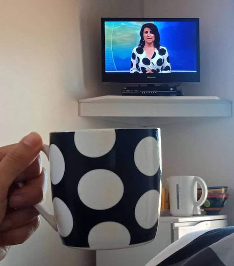 Person holding a black mug with white polka dots in front of a TV screen.