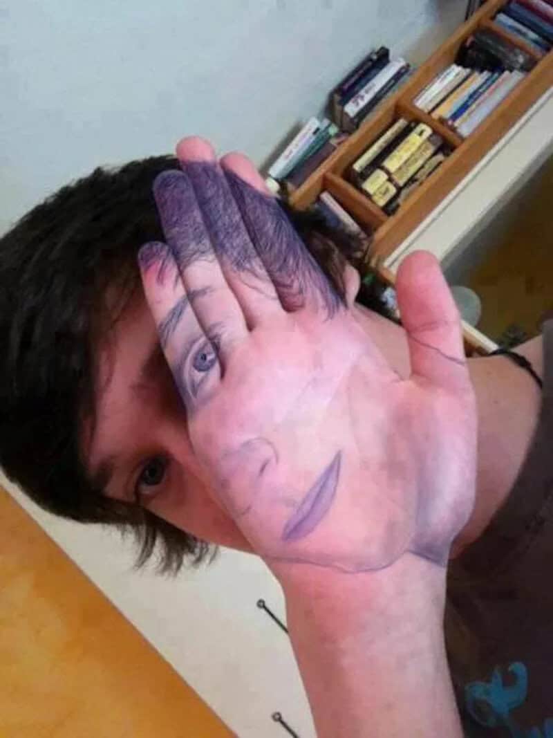 Person holding a large hand-shaped mask with a face drawn on it.