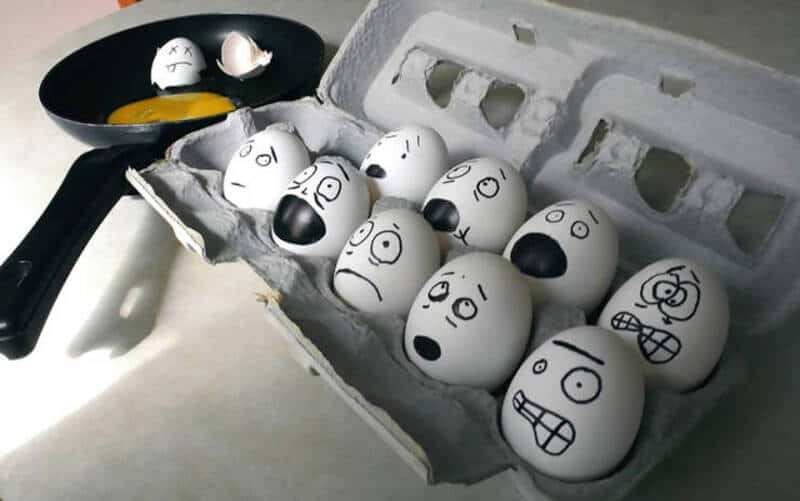 Eggs with funny faces drawn on them in a carton and a frying pan.