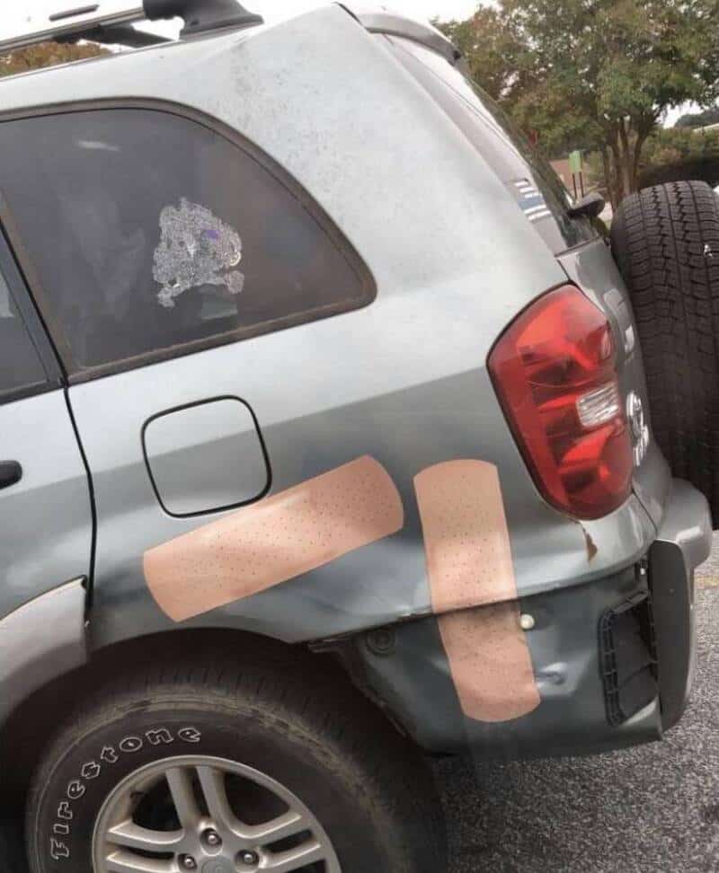 Damaged silver SUV with a large dent and two bandages on the rear side.