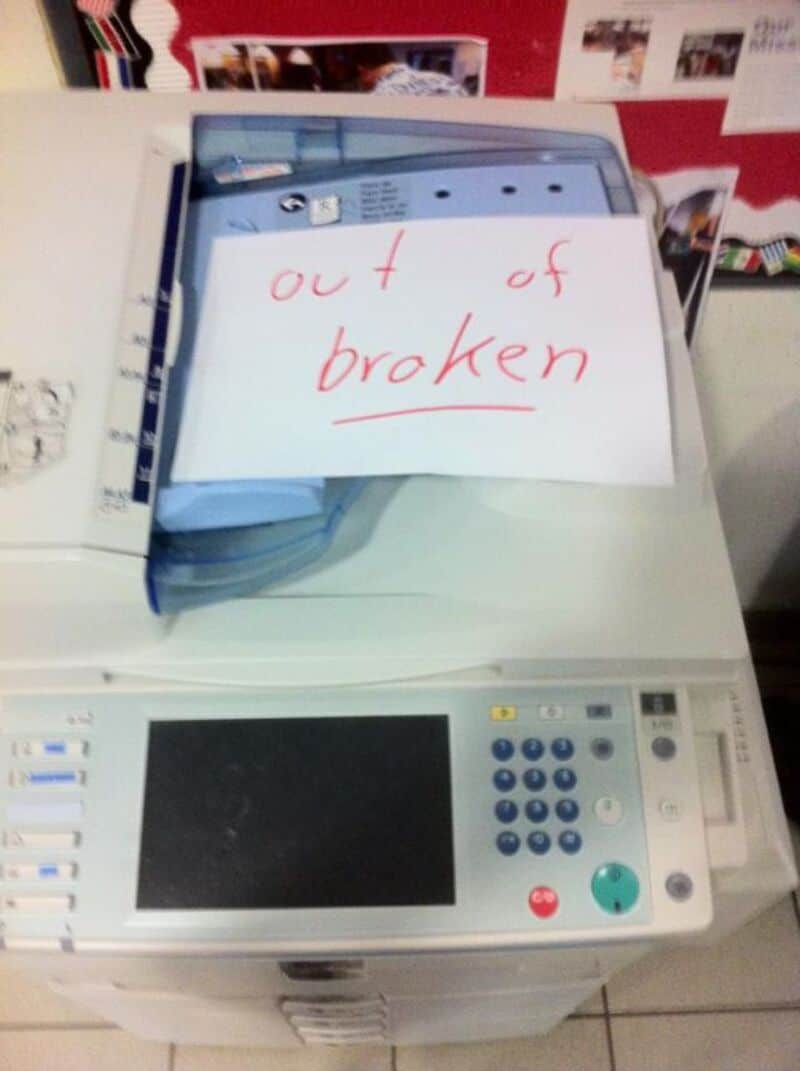 Photograph of a copier with a sign that says 'out of broken' on top.
