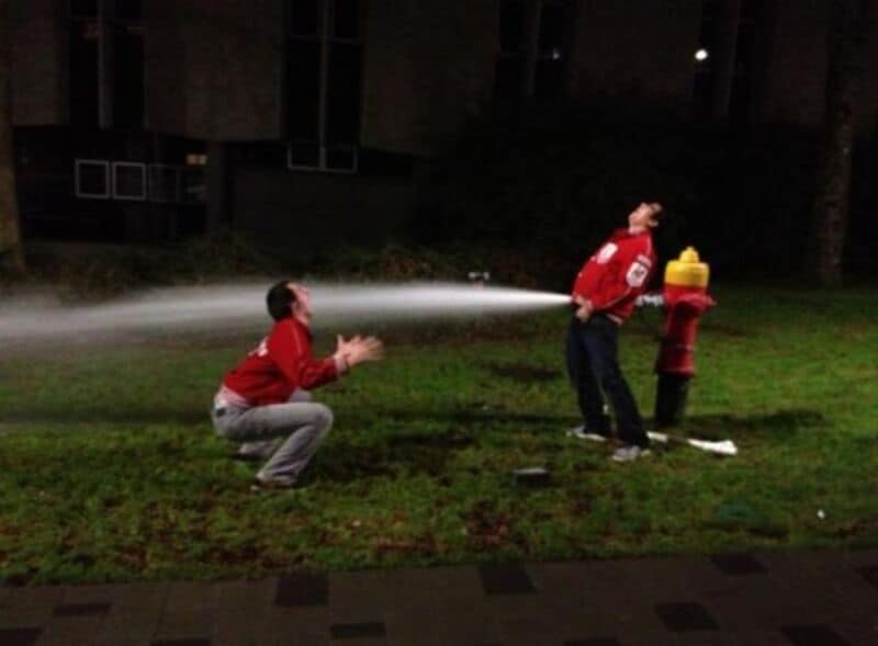 Person spraying water at another person near a fire hydrant at night.