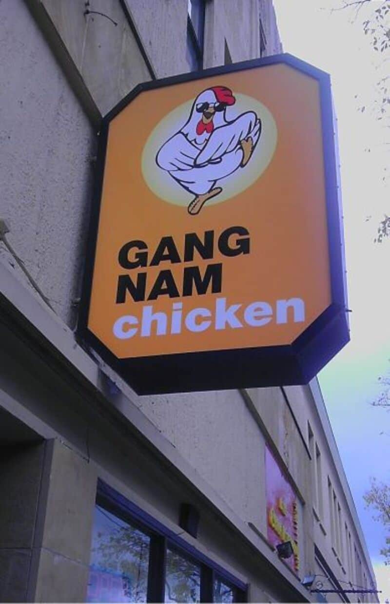 Sign for 'GANG NAM chicken' with a cartoon chicken wearing sunglasses and a red cap.