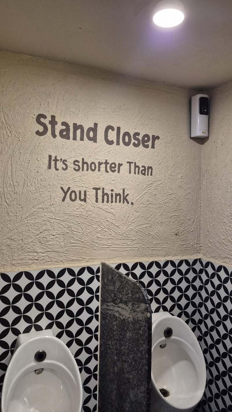 Sign in a bathroom that says 'Stand Closer It's shorter Than You Think'.